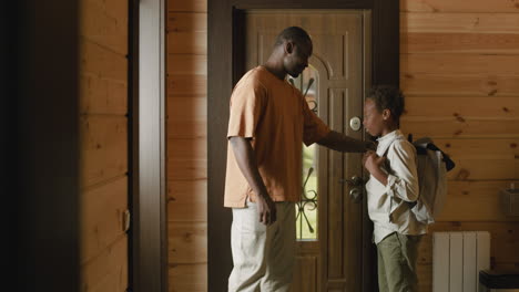 loving dad helping his son to put on school bag, then opening door and the boy leaving home