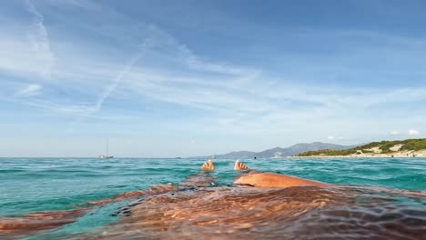 Personal-perspective-of-male-chest-legs-and-feet-relaxing-while-floating-on-azure-lagoon-of-Saleccia-famous-beach-on-Corsica-island-in-France