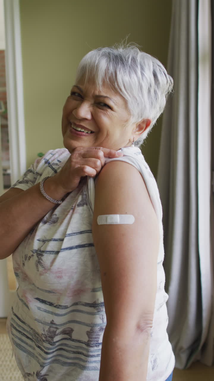 Vertical shot of a senior biracial woman showing the band-aid over vaccination spot on her shoulder
