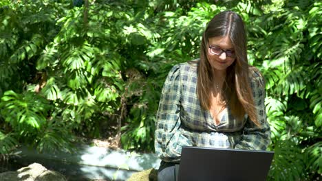 happy, smiling woman working online on a notebook on a sunny day in park