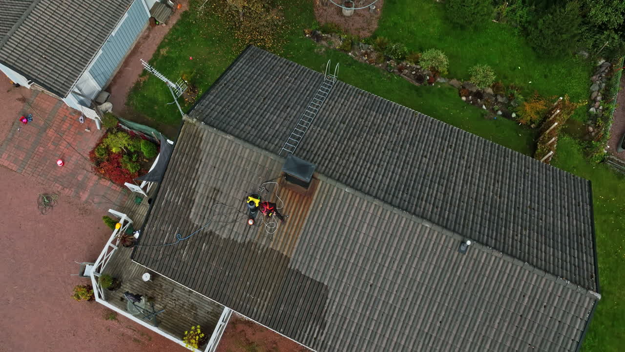 Aerial tilt shot rising above a woman pressure washing a house roof, fall day