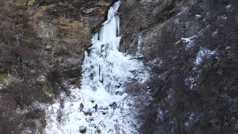 Aerial-view-of-couple-of-climbers-with-backpack-walking-towards-a-frozen-waterfall