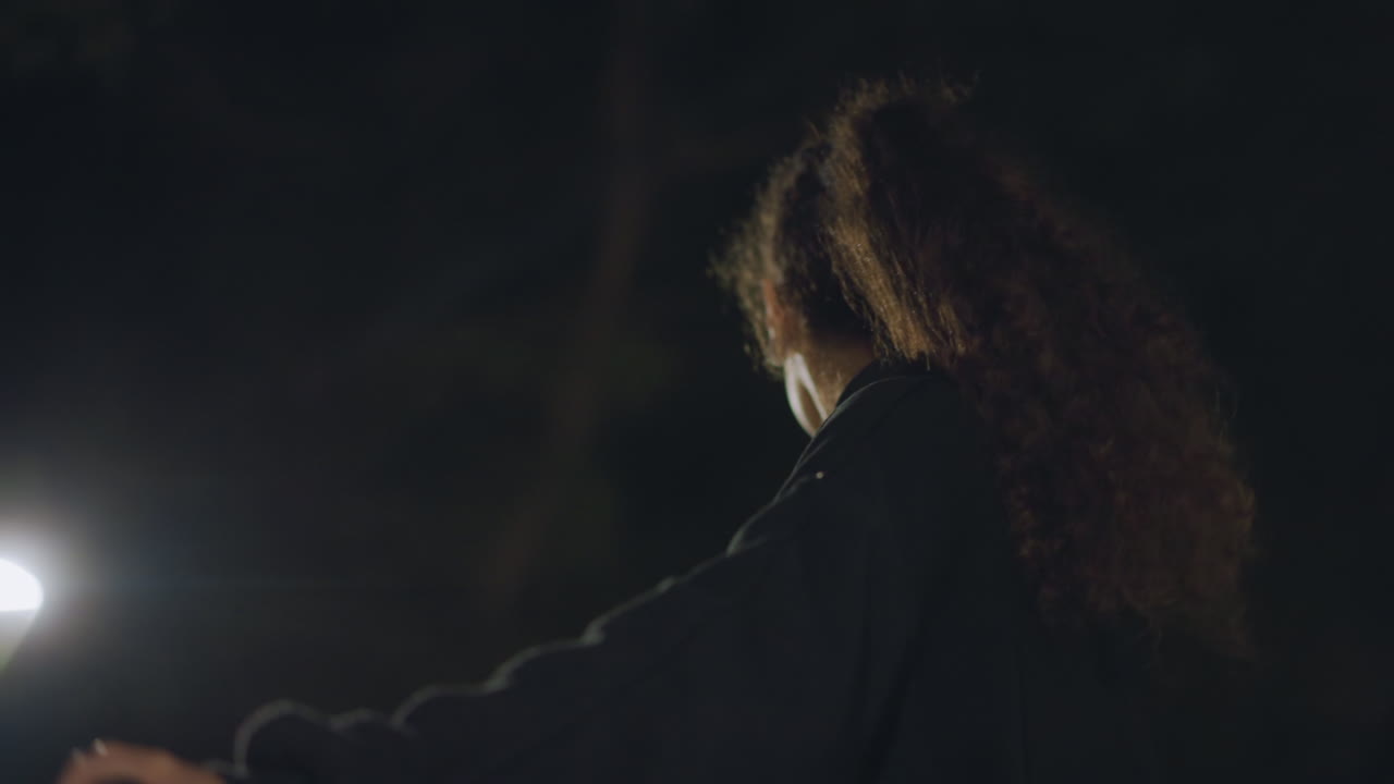 Young Woman On Bicycle From Low Angle At Night, Strong Posture With Hands On Handlebars, Park Lights Casting Dramatic Rim Glow, Sense Of Empowerment And Forward Momentum During Quiet Nocturnal Ride