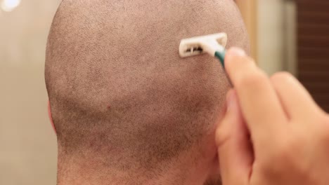 close up view of a young man shaving the back of his own bald head with a disposable razor blade