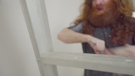 home repair man climbing down ladder mid job putting down scraper tool in focus and dusting off hands and shirt of of focus