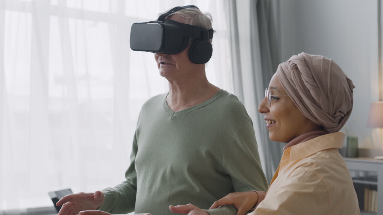 Middle Aged Arabic Woman Helping A Senior Man To Use Virtual Reality Headset Glasses At Home