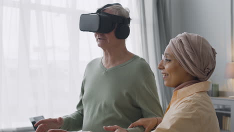 middle aged arabic woman helping a senior man to use virtual reality headset glasses at home
