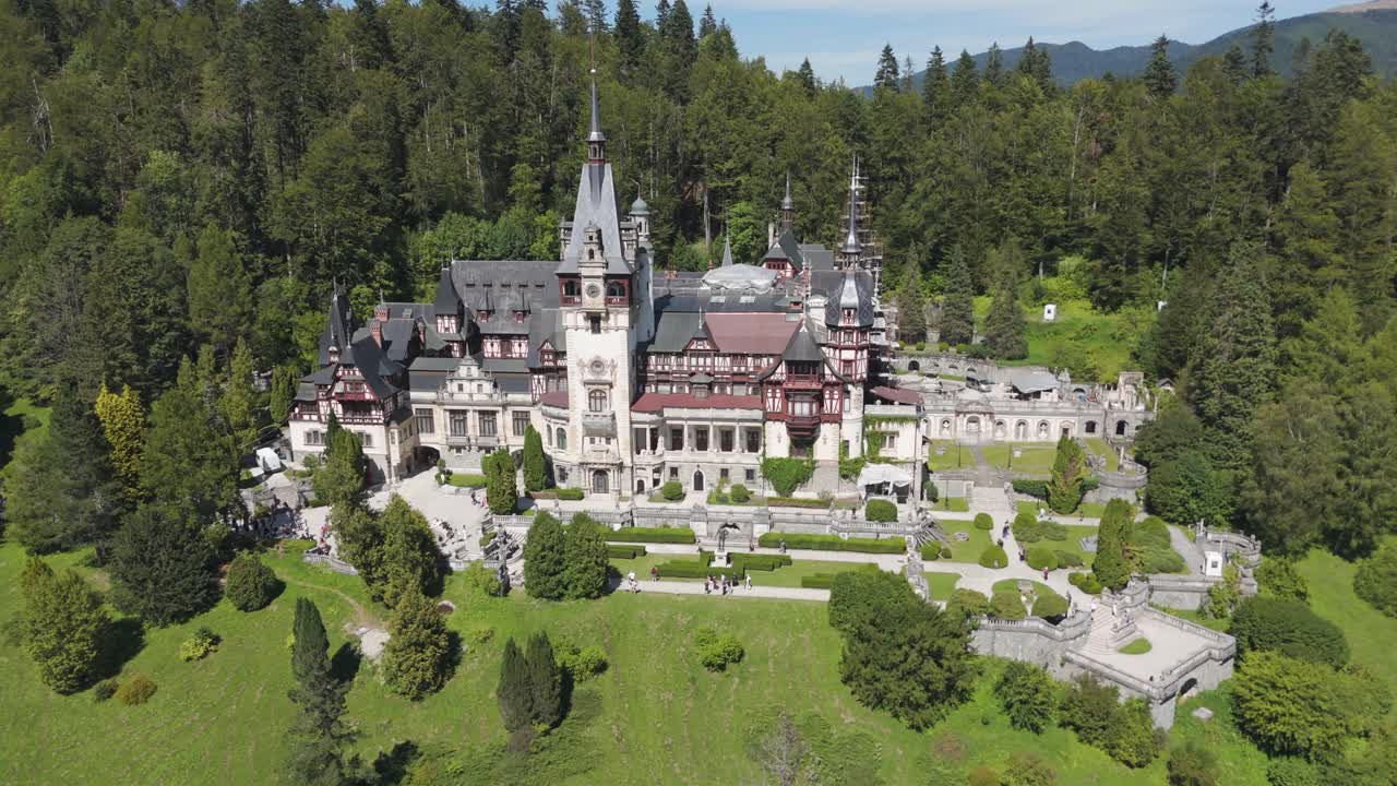 Establishing aerial shot flying toward Peleș Castle, emphasizing the historic building and dense forest landscape