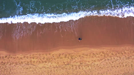 Woman-walking-on-sandy-beach-washed-by-foamy-ocean-waves-in-Thailand