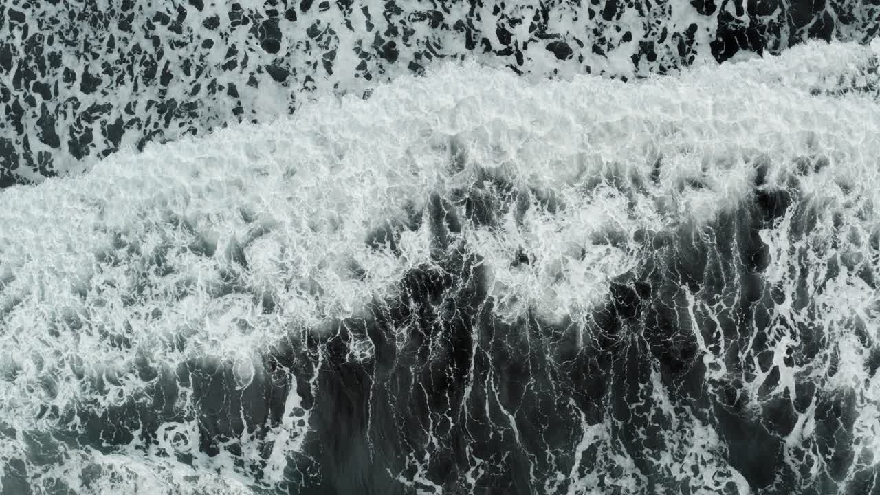 Black and white patterns of nature as wave crashes onto black sand beach