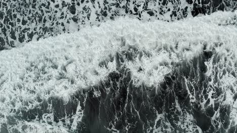 black and white patterns of nature as wave crashes onto black sand beach