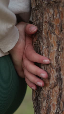 la hembra se encuentra contra el tronco de un árbol en el parque. los dedos de la mujer juegan inquietos transmitiendo una sensación de agitación interna apoyándose en la corteza. atmósfera de soledad