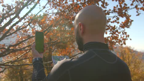 vista posterior de un joven con un teléfono móvil con pantalla verde haciendo clic en un teléfono con un mapa en las manos