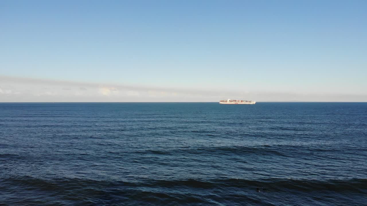 대형 화물선이 크고 탁 트인 바다를 통해 해안에서 가까운 해변 마을로 항해하며 낮게 매달린 솜털 구름을 품고 있는 아기 푸른 하늘 아래