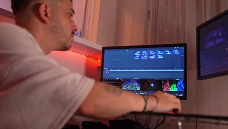 close side view of young man working intensely on video timeline and color scopes in dual monitor editing setup at home