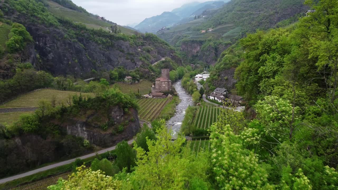 Drone view above green vineyards and a small river near Roncolo Castle in Bolzano, Italy