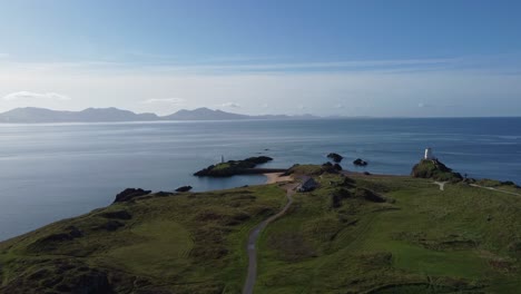 Vista-Aérea-De-La-Isla-Ynys-Llanddwyn-Y-De-La-Nebulosa-Cordillera-De-Snowdonia-A-Través-Del-Mar-Irlandés-Al-Amanecer.