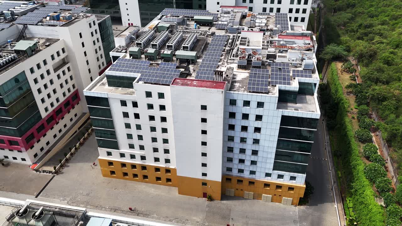 Tech Park Infrastructure: Drone footage capturing a close-up of a contemporary commercial tower within a business park. Showcases detailed rooftop mechanical units alongside extensive solar arrays