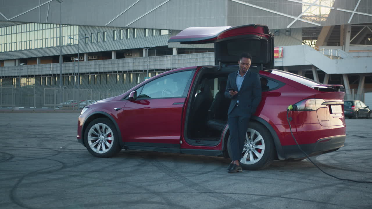 충전소 에서 전기 자동차  에 스마트폰 을 사용하는 사업가