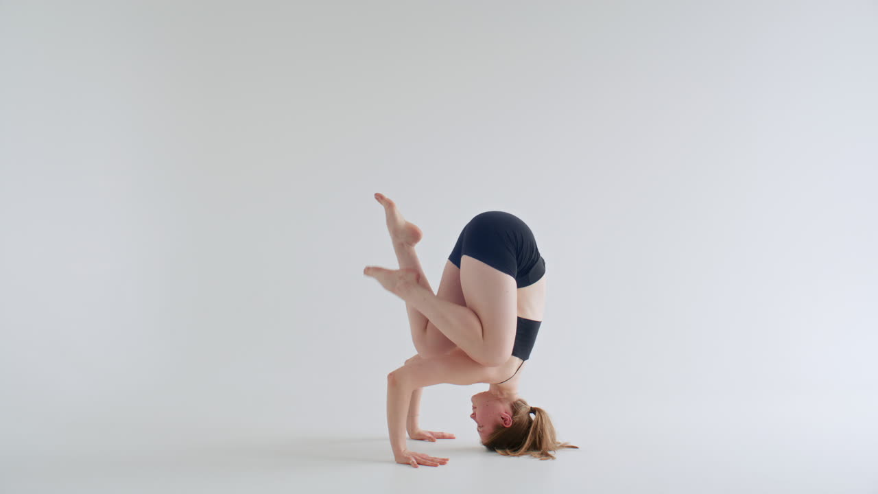 Woman Practicing Yoga Headstand and Arm Balance in White Studio