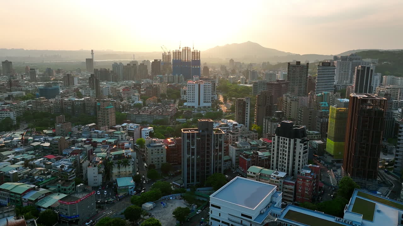 Aerial forward flight over taiwan city with skyscraper construction site at sunset - mountain range silhouette in background