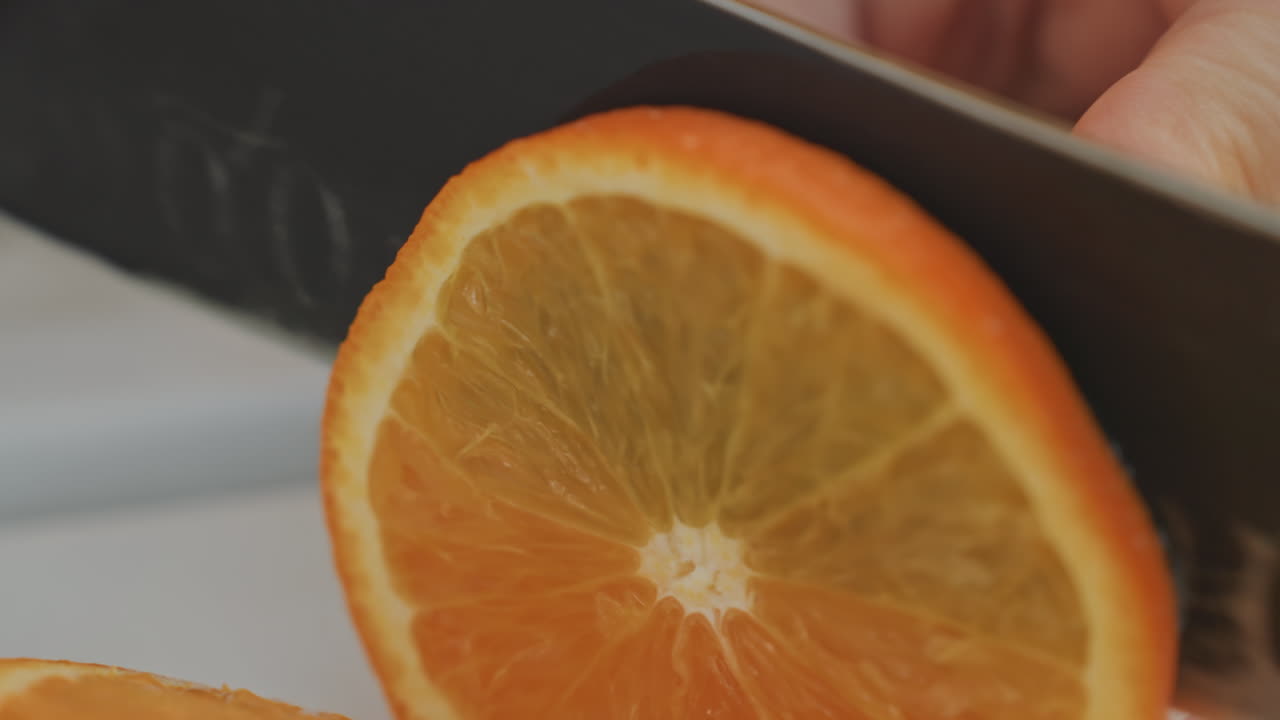 Fetta d'arancia per guarnizione da cocktail su tagliere. Taglio in stile barista con una lama affilata. Polpa vibrante e buccia lucida. Primo piano di una mano curata che tiene il frutto, con uno sfondo di cucina luminosa. Movimento preciso e pulito.