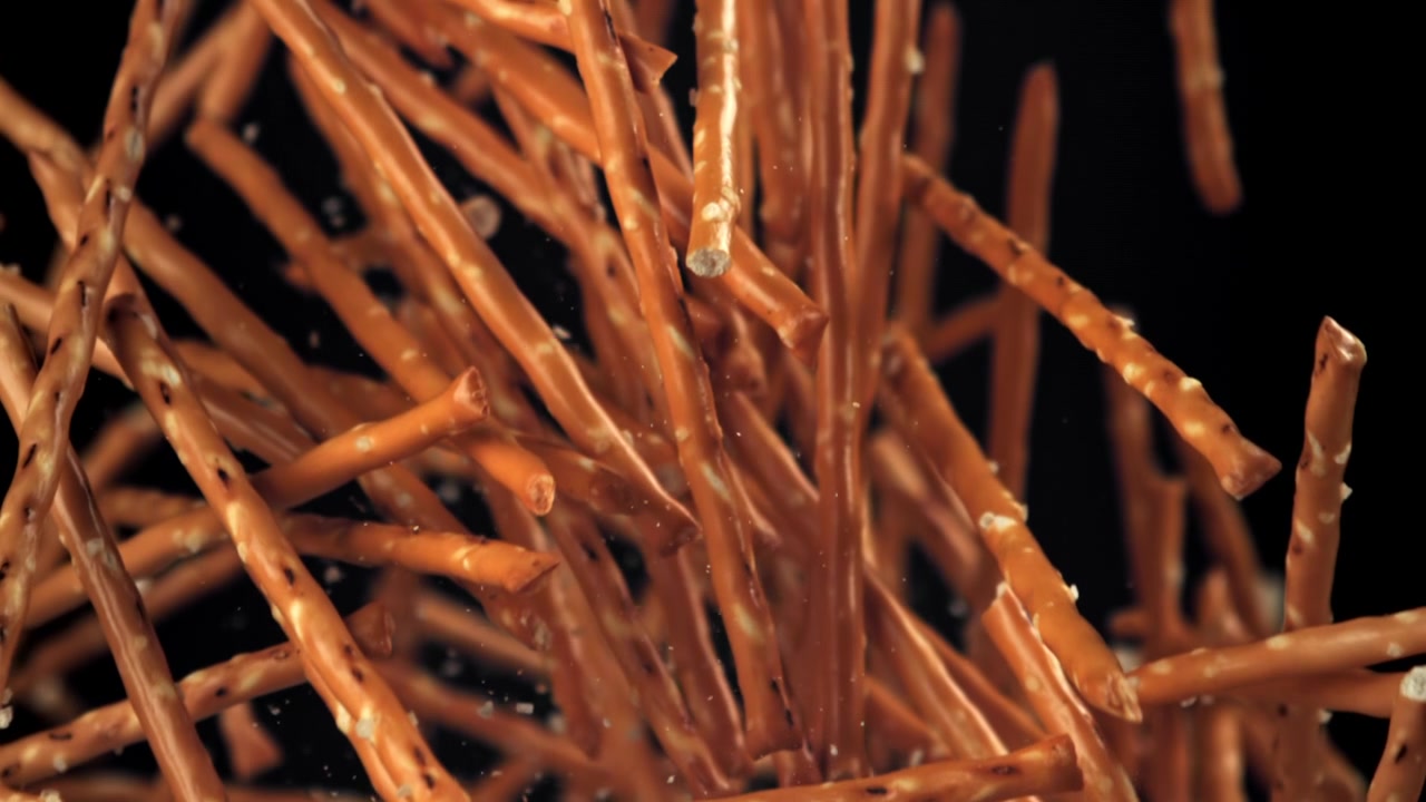 Bastoncini di pretzel salati che cadono al rallentatore su sfondo nero.