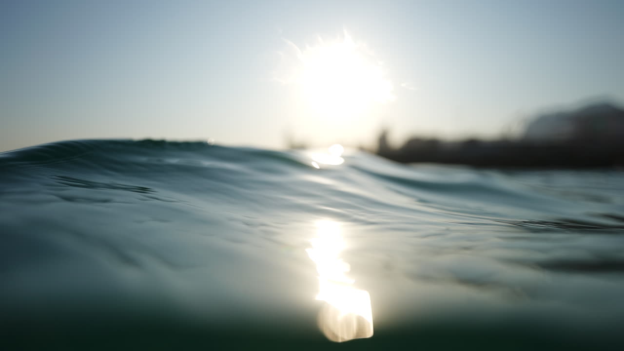 Gentle waves creating soft ripples on the ocean's surface at dawn, with sunlight reflecting brightly on the water, evoke a sense of tranquility and serene beauty in nature