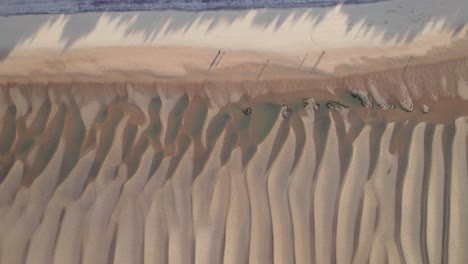 Gente-Caminando-Por-Una-Playa-De-Arena-Dorada-Al-Borde-Del-Agua-Con-Sombras