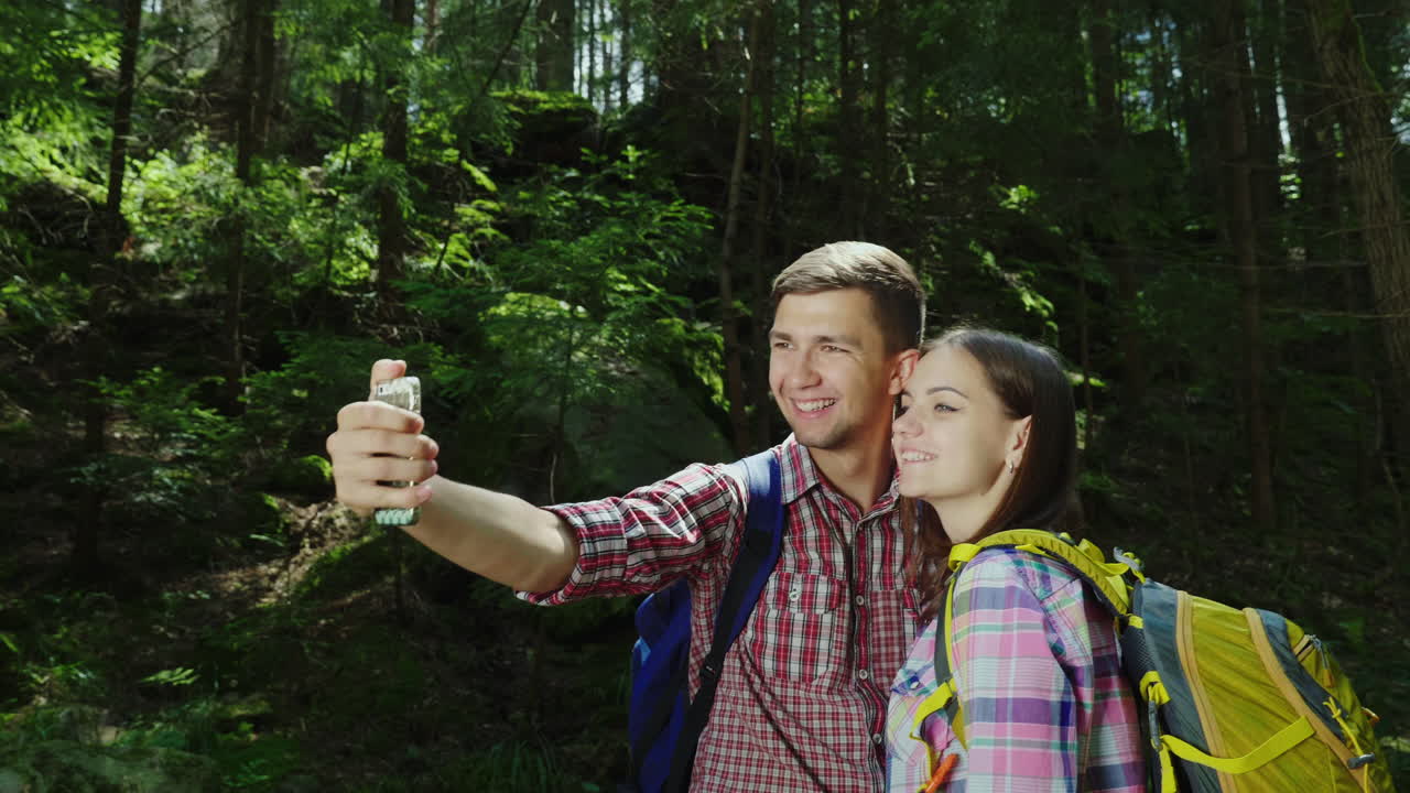 un atractivo par de turistas son fotografiados en el bosque selfie con mochilas en una caminata 4k v