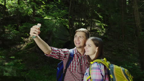 Una-Atractiva-Pareja-De-Turistas-Son-Fotografiados-En-El-Bosque-Selfie-Con-Mochilas-En-Una-Caminata-4k-V