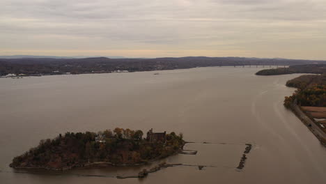 aerial drone camera flight towards bannerman's castle as it descends over the hudson river in beacon, ny on a cloudy, grey evening during sunset