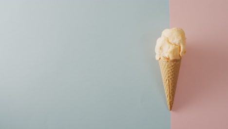 Video-of-cone-with-ice-cream-lying-on-pastel-grey-and-pink-surface