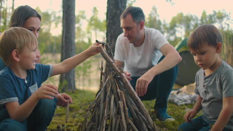 Die-Familie-Sitzt-An-Einem-Sommerabend-Am-Lagerfeuer.-Kinder-Ruhen-Sich-Mit-Ihren-Eltern-Im-Wald-Aus.-Wochenende-In-Der-Natur-In-Guter-Gesellschaft.-Familie-Brät-Würstchen-über-Einem-Feuer-Im-Wald.