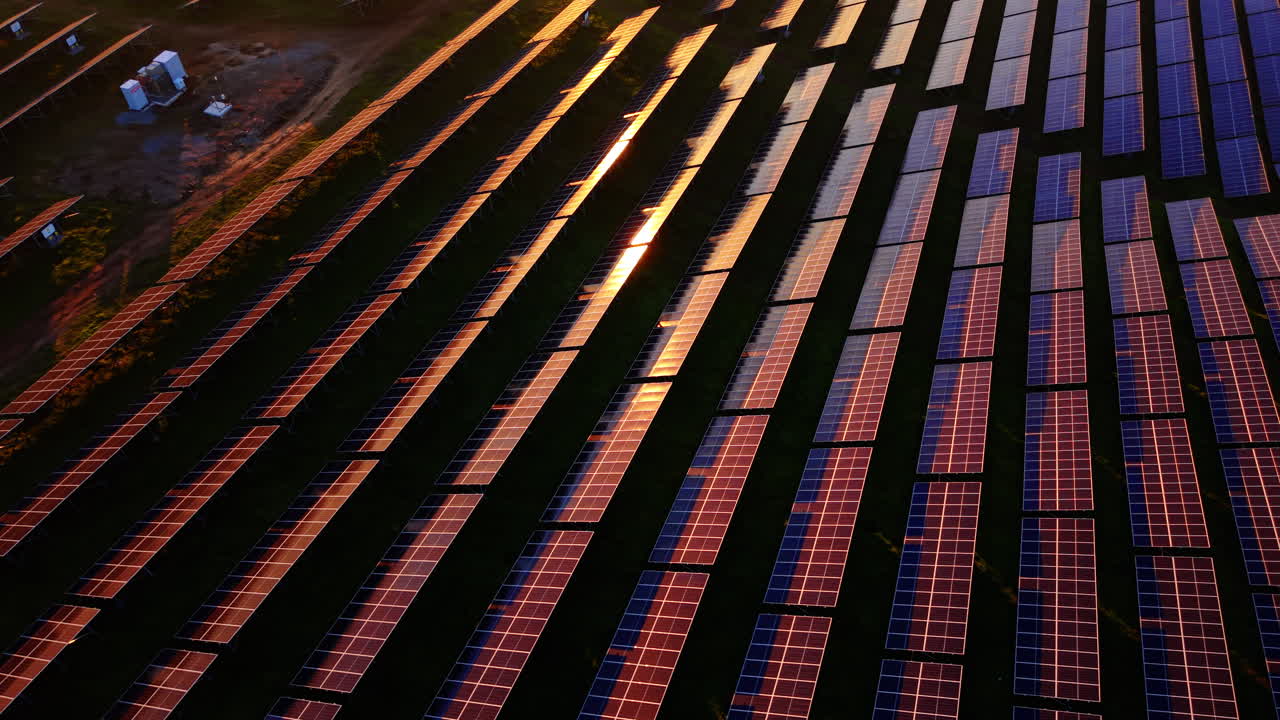 Ripresa aerea dall'alto di lunghe file di pannelli fotovoltaici con riflessi del tramonto su un prato verde. Vista dall'alto di un impianto solare.