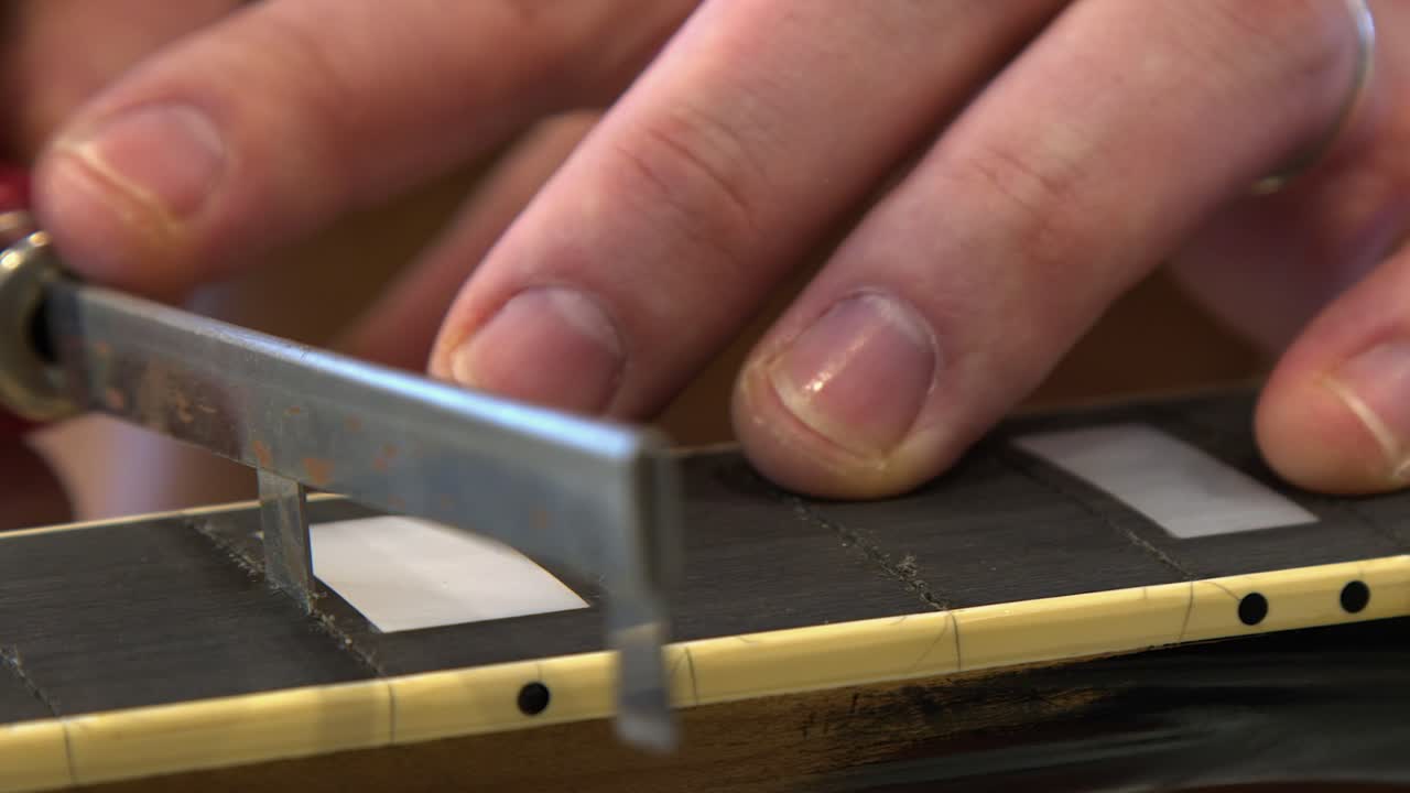 Closeup repair technician uses refret saw to channel guitar fret slots