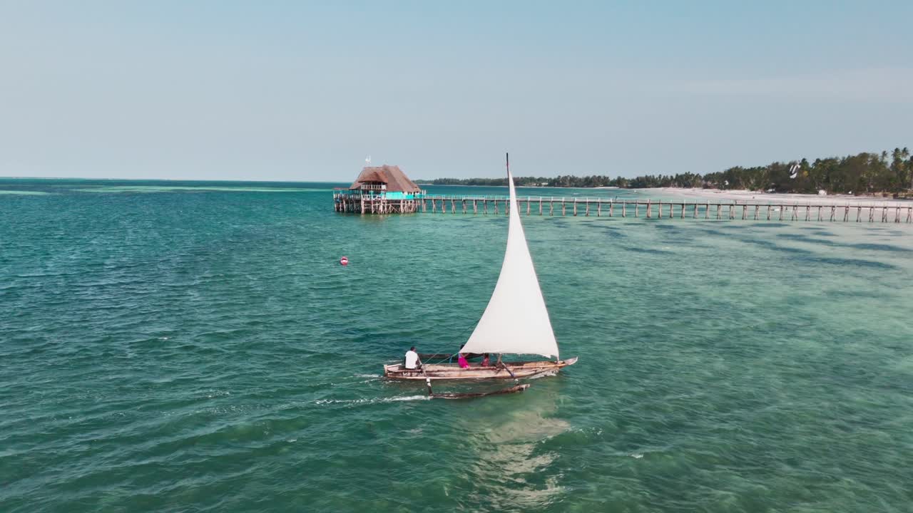 Traditional sailboat gliding over turquoise waters near a beachside pier