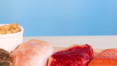 a variety of protein sources including salmon, beef, chicken, and nuts displayed on a wooden surface.