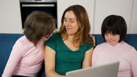 madre con dos hijas con síndrome de down sentada en el sofá divirtiéndose usando una computadora portátil