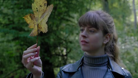 young woman stares at golden leaf in hand in woods, close-up