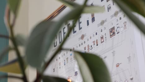 A-slow-panning-shot-of-a-coffee-poster-through-blurred-plant-leaves-beside-a-bright-window-|-Gourmet-Coffee-House-|-Shot-in-HD-at-cinematic-24-fps