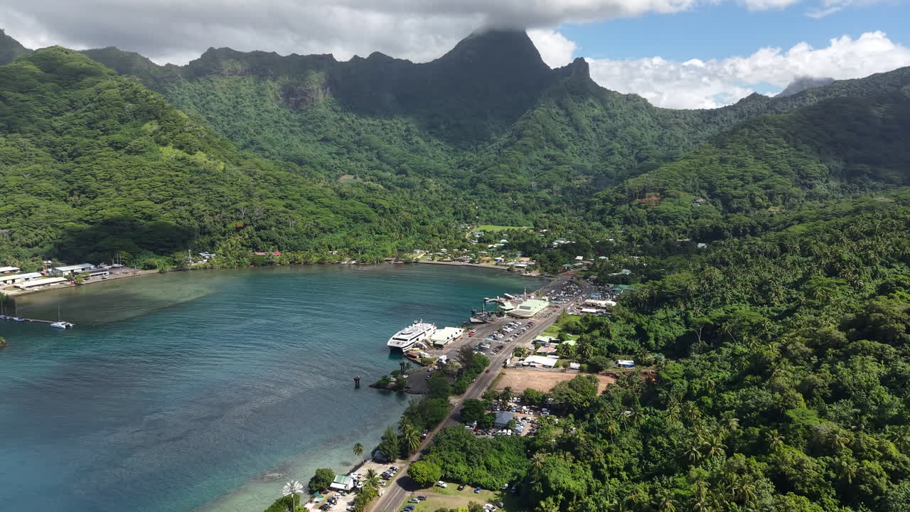 Drone Shot of Moorea Island Harbor, French Polynesia. Ferry Beat, Buildings, Coastal Road and Tropical Rainforest on Hills