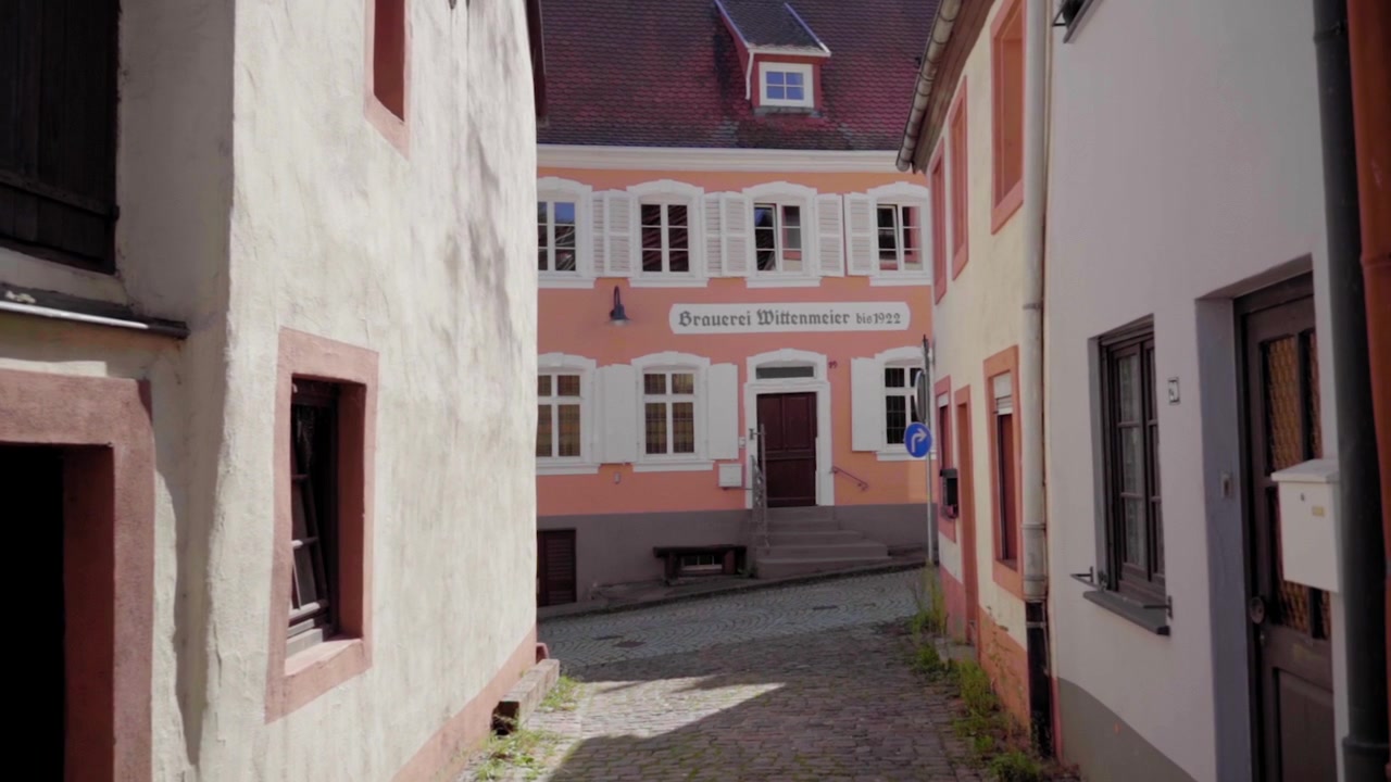 Slowmotion-optagelse af en stille tysk gyde, der fører til den historiske 'Brauerei Wittenmeier'-bygning, grundlagt i 1922. Charmerende traditionel arkitektur under sommersol.
