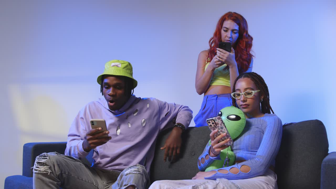 fotografía de estudio de amigos jóvenes de la generación z sentados en el sofá compartiendo publicaciones en las redes sociales en teléfonos móviles 3