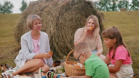 lovely family sitting on blanket enjoying fresh pastries in open field during outdoor picnic, with children and adults savoring snacks surrounded by nature