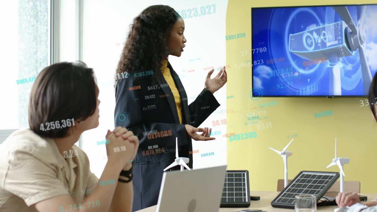 Female presenter explaining energy proposal, gesturing to monitor and models, showing data overlays