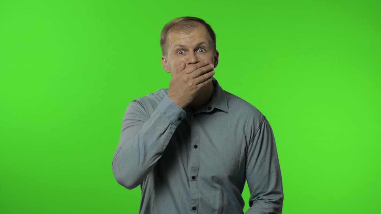 hombre aislado en fondo clave croma. cerrando la boca con la mano, gestos no, negándose a decir secreto