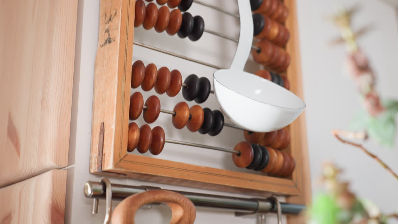 Close up of white kitchen ladle hanging on wooden vintage abacus with flower stems softly blurred in foreground, blending rustic charm and traditional decor in well-lit cozy indoor corner