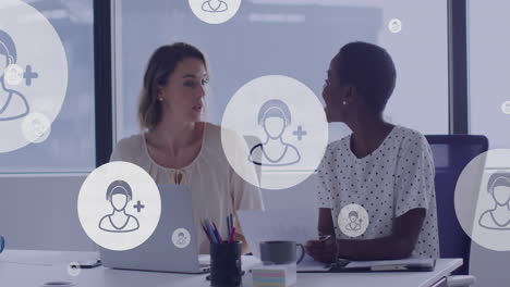 animation of people icons floating over diverse female colleagues working on laptop in office