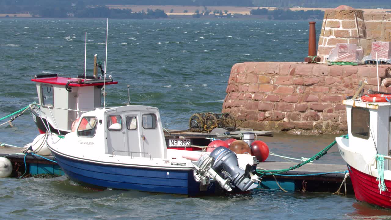 Two small fishing boats bob in choppy water beside stone pier under bright daylight